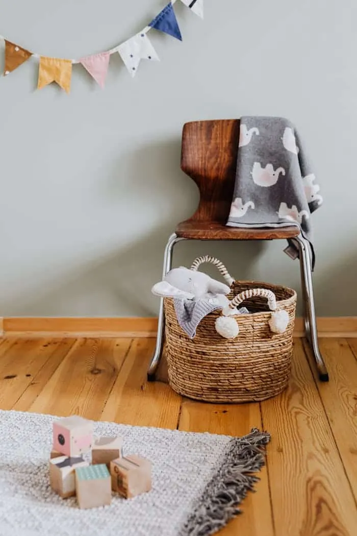 Chambre d’enfant avec chaise, panier de peluches et cubes en bois sur un tapis.