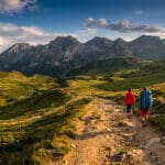 Deux randonneurs marchant sur un sentier en montagne avec en arrière-plan des sommets pyrénéens sous un ciel nuageux.